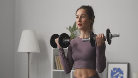 tired-sporty-woman-is-lifting-dumbbells-training-in-apartment-at-daytime-medium-portrait-of-sportswoman-at-home-during-daily-workout
